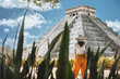 A young woman tourist in a hat stands against the background of the pyramid of Kukulcan in the ancient Mexican city of Chichen Itza. Travel concept.Mayan pyramids in Yucatan, Mexico