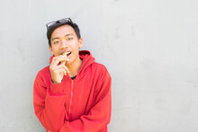 Happy Smiling Indonesian Guy With A Red Jacket Eating A Piece Of  On A White Background