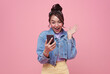 Excited Asian woman celebrating with mobile phone isolated over pink background.