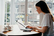 © muse studio - Surfs the Internet looking for purchases on the site. Young female freelance student working at home on a laptop. Distance learning in the apartment.