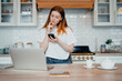 © muse studio - A female blogger is surfing the Internet on a laptop. The housewife keeps a record of expenses in the table online at home. Student beautiful girl study at home remotely.