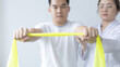 © Puwasit Inyavileart - Physical therapy, Female physiotherapist uses an elastic band to test the arm injury of a male patient attending in clinic, Bone arrangement, Non-surgical medical treatment, Medical techniques.