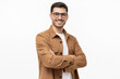 © Damir Khabirov - Young hispanic man wearing brown shirt and glasses, looking at camera with positive confident smile, holding arms crossed, isolated on gray background