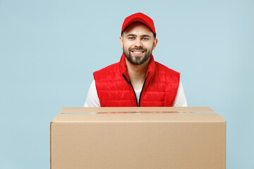 Wall Mural - Professional delivery guy employee man in red cap white T-shirt vest uniform workwear work as dealer courier hold blank cardboard box isolated on pastel blue color background studio. Service concept.