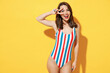 Happy young sexy woman slim body wear red blue one-piece swimsuit showing victory sign v-sign gesture isolated on vivid yellow color wall background studio. Summer hotel pool sea rest sun tan concept.