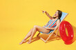 © ViDi Studio - Full body length happy young sexy woman wear striped red blue one-piece swimsuit sit on wooden chair isolated on vivid yellow color wall background studio. Summer hotel pool sea rest sun tan concept.