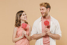 Young Parent Man With Child Teen Girl Wear Casual Clothes Daddy Kid Daughter Hold Red Sweet Candy Lollipop Looking To Each Other Isolated On Beige Background Studio. Father's Day Love Family Concept