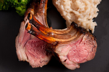 Poster - Gourmet rack of lamb chops with risotto and vegetables on a black background