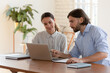 © fizkes - Businessman mentor teaching smiling female trainee, helping with corporate software, using laptop, pointing at screen, team working together, analyzing business project result, discussing data