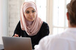 © fizkes - Beautiful Asian muslim businesswoman wearing hijab talking with colleague at meeting close up, diverse employees discussing business project strategy, attentive female leader listening ideas