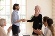 © fizkes - Confident businessman executive shaking Asian muslim businesswoman hand at meeting, team leader greeting new employee or thanking successful worker for good work result, congratulating promotion