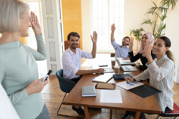 Canvas Print - Successful smiling diverse employees team with middle aged business coach mentor raising hands, voting at meeting, colleagues discussing project strategy or plan in boardroom, staff training