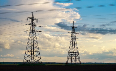 High voltage lines and power pylons in a flat and agricultural landscape on a sunny day with clouds in the blue sky.