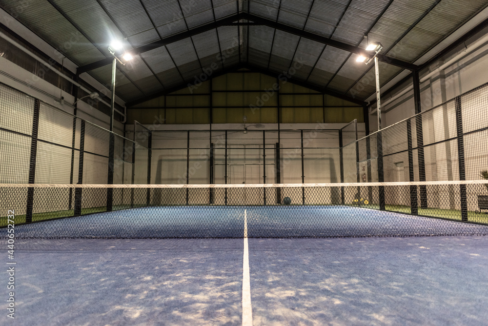 empty paddle tennis court with lights on in a covered shed with no players - obrazy, fototapety, plakaty 