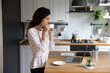 © fizkes - Confident woman drinking coffee, looking at laptop screen, watching video in social network, holding white cup and standing in kitchen, businesswoman enjoying morning, starting new workday