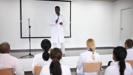 Wall Mural - Portrait of confident successful male coach in face mask for disease protection giving speech at medical conference. High quality FullHD footage