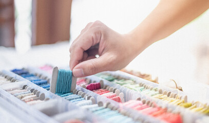 Wall Mural - Close up hands of tailor woman holding ocean blue threads and different colors in the box put on the table and prepare to use with white cotton and frame wood.