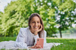 © baranq - Beautiful woman using mobile phone in park lying on blanket