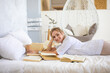 © dtatiana - Beautiful sensual young woman with blonde hair wearing a white shirt reading books and drinking coffee on the bed in modern home