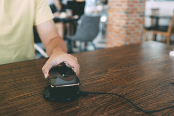 Wall Mural - Charging mobile phone battery with wireless device in the table. Smartphone charging on a charging pad. Mobile phone near wireless charger.