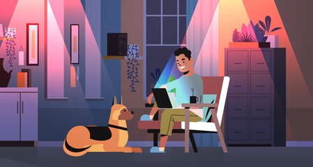 Wall Mural - overworked businessman freelancer looking at laptop screen man with dog working in dark night home room