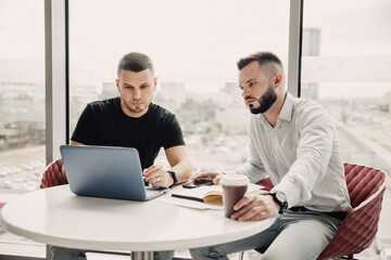 two colleagues or business partners sitting at table in the office, watching on laptop and discussin