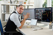 © DragonImages - Portrait of cheerful trader sitting at his office desk with various charts and stock market data on computer screen