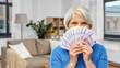© Syda Productions - savings, finances and people concept - senior woman hiding her face behind fan of five hundred euro money banknotes over home living room background