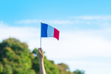 hand holding France flag on blue sky background. holiday of French National Day, Bastille Day and happy celebration concepts