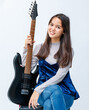 © Bangkok Click Studio - Portrait shot of an attractive smiling young Thai-Turkish teenager sitting and holding the electric guitar on the amplifier. Junior girl guitarist looking at the camera isolated in white background