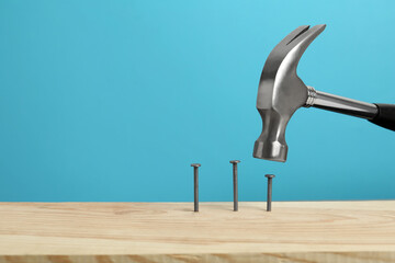 Hammering nail into wooden surface against light blue background, space for text