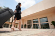 © DragonImages - Young businesswoman in high heels pulling suitcase when walking to entrance of hotel building