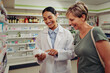 Young female pharmacist and customer reading ingredients and dosage in pharmacy standing near shelves
