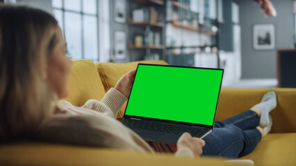 Aufkleber - Beautiful Caucasian Specialist Working on Laptop with Green Screen Mock Up Display at Home Living Room while Lying on a Couch Sofa. Freelance Female Chatting Over the Internet on Social Networks.