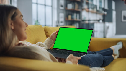 Aufkleber - Beautiful Caucasian Specialist Working on Laptop with Green Screen Mock Up Display at Home Living Room while Lying on a Couch Sofa. Freelance Female Chatting Over the Internet on Social Networks.