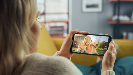 Poster - Close Up of a Female Chatting in a Video Call with Her Beautiful Friend Playing with a Dog on Smartphone from Home Living Room. Freelancer Chatting with a Client on a Call Over the Internet.
