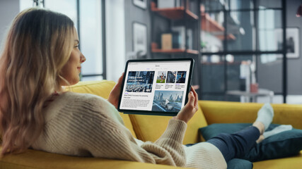 Aufkleber - Beautiful Authentic Female Using Tablet Computer for Reading Latest News and Articles about Technology. She is Lying on a Couch at Home Living Room. Freelancer Working From Home, Surfing the Internet.