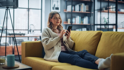 Aufkleber - Beautiful Caucasian Female Using Smartphone in Stylish Living Room while Resting on a Cozy Couch Sofa. Young Woman at Home, Browsing Internet, Using Social Networks, Having Fun in Flat.
