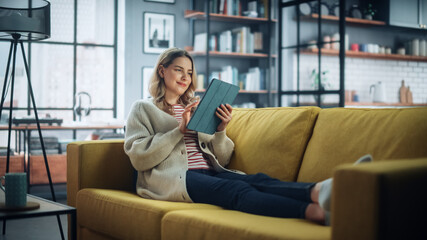 Fototapete - Beautiful Caucasian Female Using Tablet Computer in Stylish Living Room while Resting on a Cozy Couch Sofa. Young Woman at Home, Browsing Internet, Using Social Networks, Having Fun in Flat.
