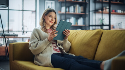 Aufkleber - Beautiful Caucasian Female Using Tablet Computer in Stylish Living Room while Resting on a Cozy Couch Sofa. Young Woman at Home, Browsing Internet, Using Social Networks, Having Fun in Flat.