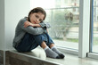 © New Africa - Sad little girl sitting on window sill indoors