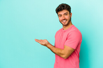 Young caucasian man isolated on blue background holding a copy space on a palm.