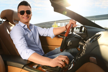 Businessman driving luxury convertible car outdoors on sunny day