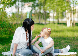 happy little girl and her mother having fun outdoors on the green grass in sunny summer day