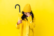 © luismolinero - Asian woman with rainproof coat and umbrella isolated on yellow background with tired and sick expression