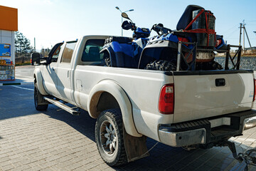 White pick-up truck loaded with ATV near gas station