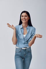 Wall Mural - Attractive young woman looking at camera and smiling while standing against grey background