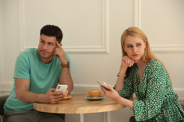 Poster - Displeased man and young woman with smartphones in cafe. Failed first date