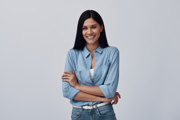 Wall Mural - Attractive young woman looking at camera and smiling while standing against grey background