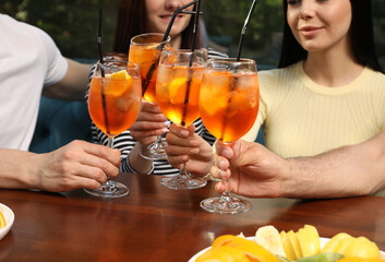 Wall Mural - Friends clinking glasses of Aperol spritz cocktails at table, closeup